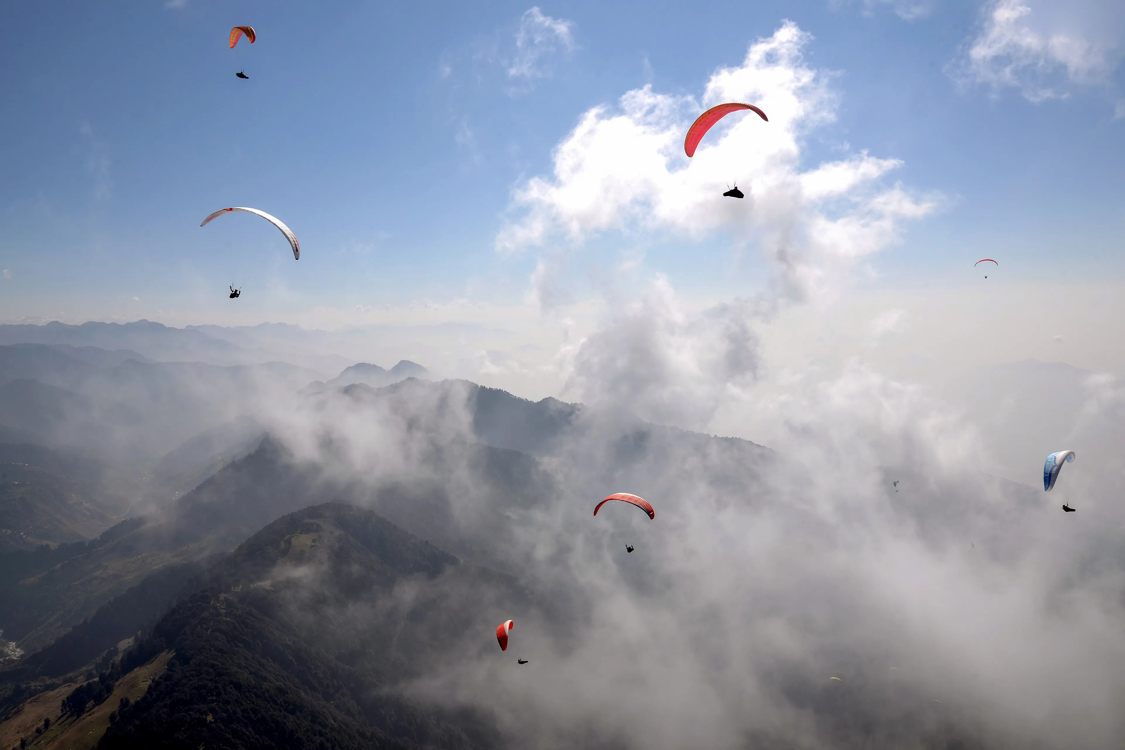 A paraglider soaring above the Dhauladhar range at Bir Billing